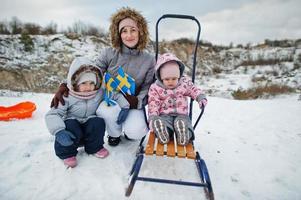 mamma med döttrar håller sverigeflaggor i svenska vinterlandskap. foto