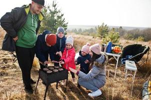 stor familj med fyra barn som grillar på ett däck i tallskogen. grilldag med grill. foto