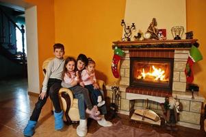 glada fyra barn hemma vid en öppen spis i varma vardagsrummet på vinterdagen. foto