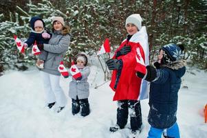 mamma med barn som håller Kanadas flagga på vinterlandskap. foto