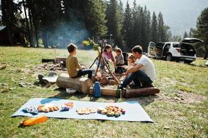 familjens bål i berget. steka korv. fyra barn camping. höstvandring och lägerväder. uppvärmning och matlagning nära lågan tillsammans. foto