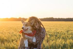 ung glad kvinna med dreadlocks leka med corgi hund i sommar vetefält foto