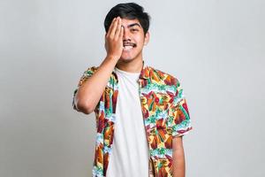 asiatisk man som bär casual casual strandskjorta som täcker ena ögat med handen foto
