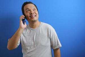 foto av en fet asiatisk man som bär en grå skjorta som ler medan han tar emot en telefon