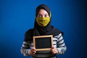 porträtt av ung asiatisk kvinna som bär skyddsmask mot coronaviruset, håller liten svart tavla foto