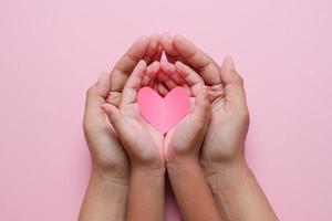 vuxna och barn händer som håller rött hjärta över rosa bakgrund. kärlek, sjukvård, familj, försäkring, donationskoncept foto
