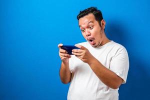 asiatisk kille som bär en vit t-shirt ser förvånad över de goda nyheterna han fick från sin smartphone foto