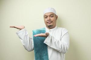 porträtt av asiatisk ung muslimsk man som ler och pekar på att presentera något på sin sida foto