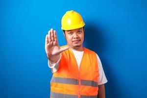 fet asiatisk arbetare som bär orange säkerhetsväst och gul hjälm gör stoppgest foto