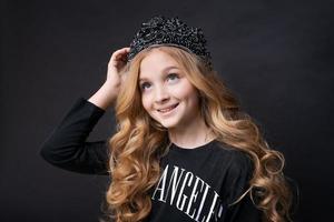 vacker liten prinsessflicka i svarta kläder med en krona på huvudet poserar foto