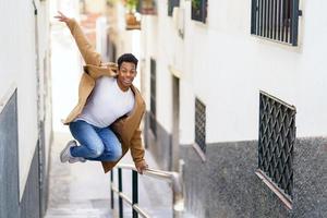 ung svart man hoppar av glädje över en ledstång på gatan. foto