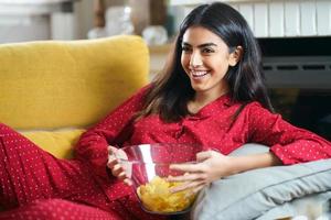 persisk kvinna hemma tittar på tv äter chips potatis foto