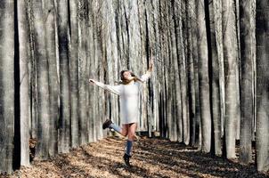 vacker blond tjej, klädd med beige klänning, hoppar in i skogen foto