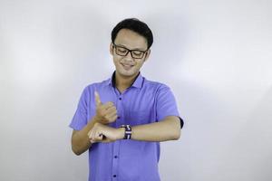ung asiatisk man bär blå skjorta är glad och ler när han pekar och tittar in i klockan isolerad över vit bakgrund foto