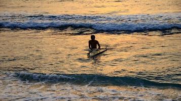 dokumentation av surfare i aktion i skymningen med en gyllene färg och mörk, ofokuserad och mörk på stranden i senggigi lombok, västra nusa tenggara, Indonesien, 27 november 2019 foto