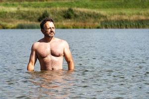 En medelålders sportig man badar i den lilla förortssjön på sommaren foto