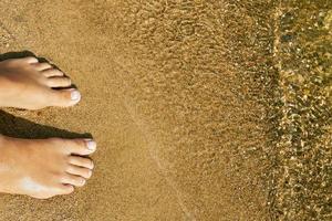 tonårsflickans bara fötter står på sanden på en sjöstrand nära vattnet foto