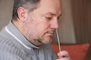 man samlar nässlemprov från näsan med en bomullspinne för självtestning av covid-19 coronavirus hemma foto