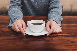 kvinnans hand som håller en kaffekopp på ett träbord foto