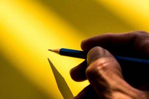 människans hand håller penna för att skriva på papperet i skuggan foto