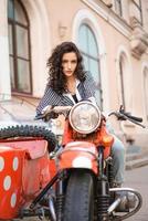 flickan sitter på en motorcykel mot bakgrund av staden. foto