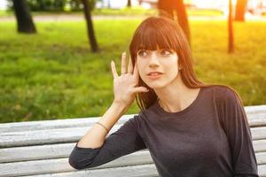 ung kvinna i parken håller en hand nära örat, begreppet avlyssning foto