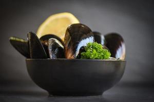 råa musslor med örter citron på skål och mörk bakgrund - färska skaldjursskaldjur på is i restaurangen eller till försäljning på marknaden musselmat foto