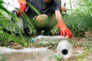 pojke man hand plocka upp plastflaska i skogen. miljö koncept. foto