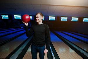 glad ung man som håller ett bowlingklot stående mot bowlingbanor med ultraviolett ljus. foto