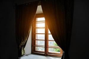trä antika fönster med gardiner i mörkt rum med solljus foto