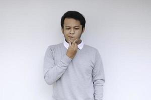ung asiatisk man bär grå skjorta med tänkande och letar idé gest foto