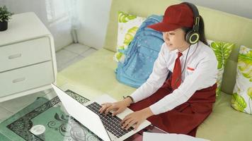 asiatisk grundskolflicka studerar online hemma att skriva medan du lyssnar foto