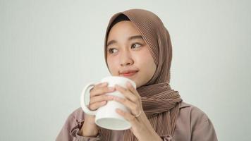 asiatisk kvinna i hijab funderar på inspiration medan hon njuter av en drink hemma foto