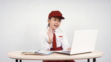 asiatisk grundskola flicka hälsning till laptop skärm isolerad på vit bakgrund foto