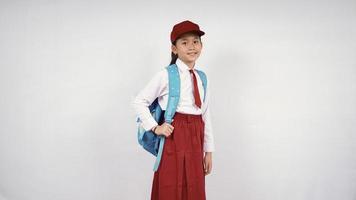 asiatisk liten flicka som bär hatt och skolväska ler glatt på vit bakgrund isolerad foto