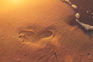 fotspår i sanden på stranden vid solnedgången foto
