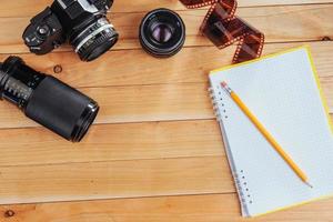 den gamla filmkameran och rullfilmen och anteckningsboken med penna på en träbakgrund foto