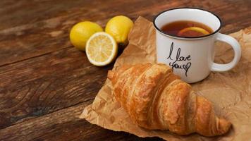 färska croissanter och en kopp te med citron på ett träbord. toppvy foto