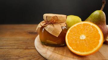 glasburk med hemgjord päron- och apelsinmarmelad med färsk frukt på bordet foto