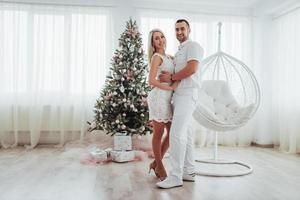lyckligt ungt par vid jul, vackra presenter och träd i bakgrunden foto