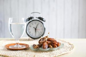 glas dricksvatten och dadlar med väckarklocka som visar klockan 6. traditionell ramadan, iftarmåltid. iftar tidskoncept foto