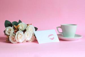 kopp kaffe med ros och kyss markerad på vitt kuvert isolerad på rosa bakgrund foto
