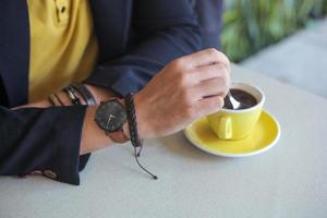 hand av män som bär klockor och armband rör om kaffet i en kopp foto