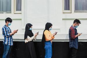 grupp unga människor som väntar på att gå in på en butiksmarknad samtidigt som de håller socialt avstånd i kö under coronatiden - livsstil för stadsutbrott, skyddande ansiktsmask och spridningsvirusförebyggande foto