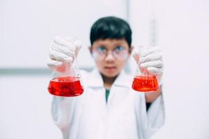 en elev som visar röd vätska i bägaren. utföra experiment i ett laboratorium. nationella vetenskapsdag, världsvetenskapsdag foto