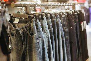 suddigt foto av olika jeansbyxor som hänger på galgarkläder inne i butiken