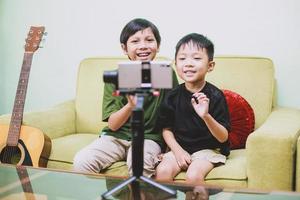 två asiatiska barn som ler och interagerar med smart telefon medan de gör videosamtal foto