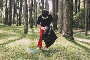 en pojke plockar upp plastflaskor i det gröna gräset i skogen foto