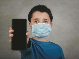 barn som bär medicinsk mask med smartphone foto