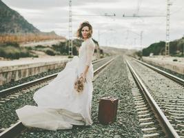 eftertänksam brud med en röd resväska på tågspåren foto
